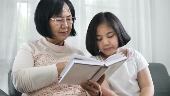 Happy Asian grandmother and lovely girl reading book together.