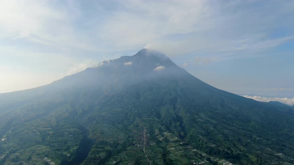 Majestic volcano Mount Merapi peak over serene Wonolelo village, Indonesia, aerial view