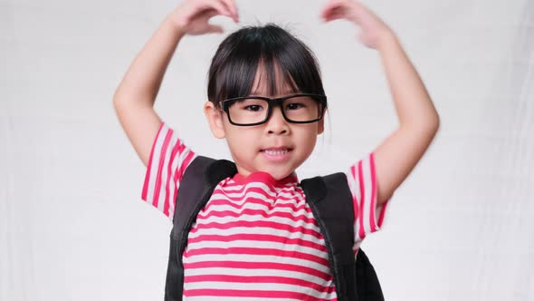 Happy schoolgirl wearing casual clothes with a backpack and doing heart-shaped hands on her