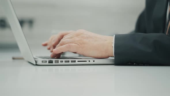 Unrecognizable Senior Man Is Using a Laptop and Typing at the Keyboard. Businessman Is Sitting at