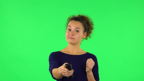 Portrait of Curly Woman with TV Remote in Her Hand, Switching on TV. Green Screen