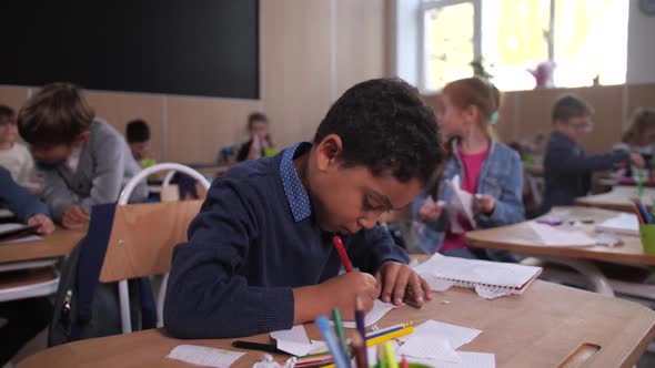 Curly Mixed Race Schoolboy Drawing in Classroom