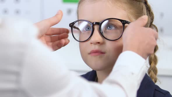 Happy Girl Putting on Eyeglasses Prescribed by Doctor, Looking in Mirror, Health