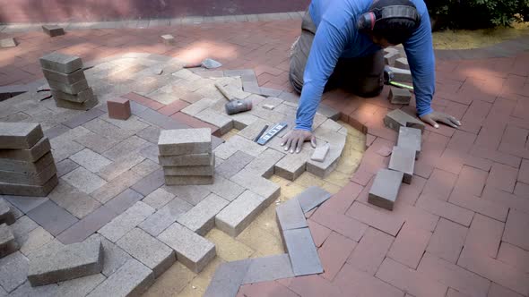 Brick paver artisan wearing ear protection marches over with freshly cut brick wedge, puts it into p