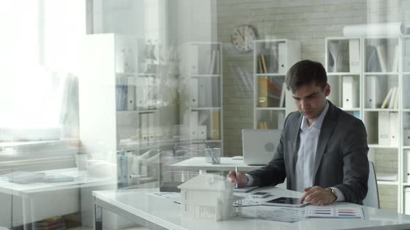 Caucasian Architect Using Digital Tablet and Taking Notes at Office Desk