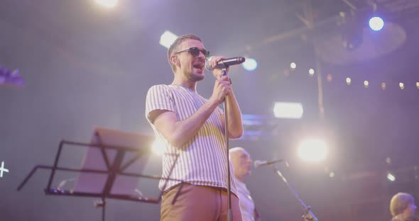 Young Man in Striped Tshirt and Black Glasses Performs on Stage with a Band