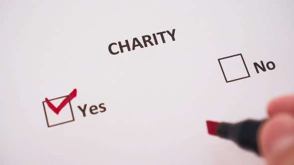 The hand ticks the word YES under the word CHARITY with a red marker 