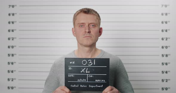 Portrait of Adult Man Holding Cardboard While Being Photographed in Police Department