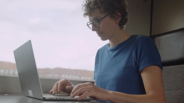 Woman in Glasses Working on a Laptop While Going By Train