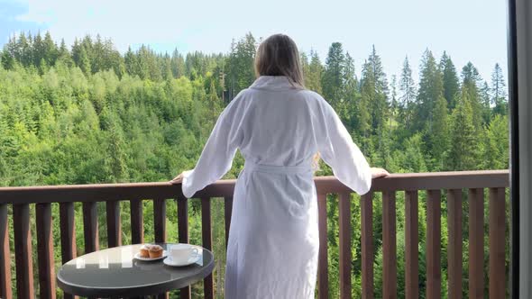 Beautiful Young Woman in Bathrobe Standing on Hotel Terrace or Balcony and Looking on the Pine