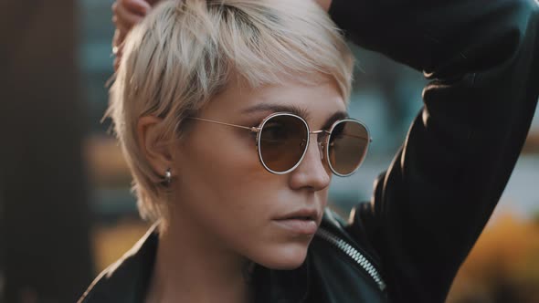 Close Up Portrait of Joyful Young Woman with Bright Hair and Sunglasses Standing Alone in Park