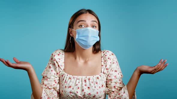 Young Pretty Unsure Woman in Protective Mask Shrugs Arms, Makes Gesture of I Don't Know, Can't Help