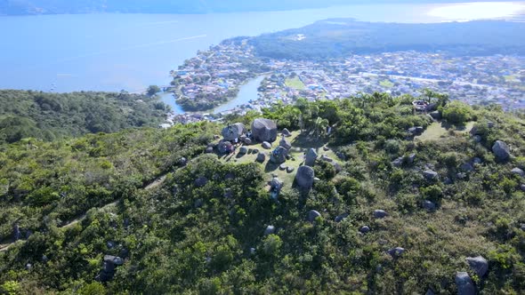 Aerial drone scene of mountain with rocks on top with city between ocean and river in background