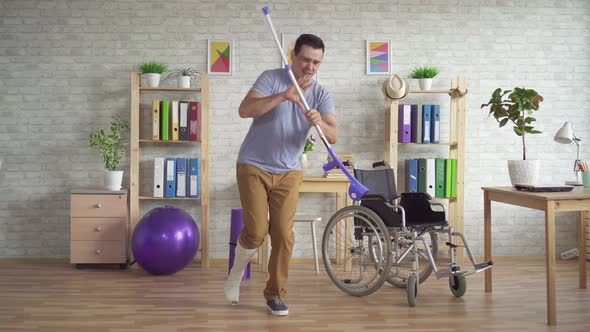 Cheerful Expressive Man with a Broken Bandaged Leg Plays Crutches Like a Guitar