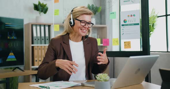 Businesswoman in Wireless Headset Has Pleasant Conversation Via Video Chat while Working