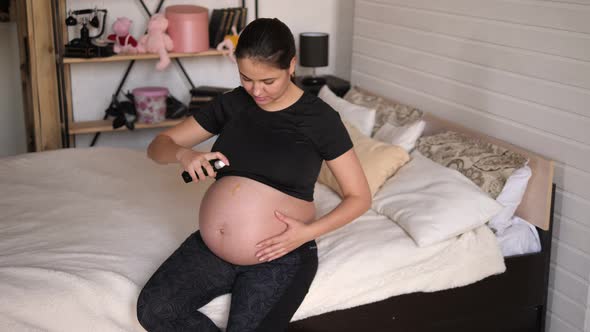 Pregnant Woman is Applying Moisturizing Body Oil on Her Belly