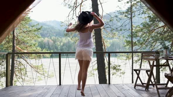 Young Woman in Shorts, a T-shirt and a Black Hat Dancing on a Terrace with Mountain Views