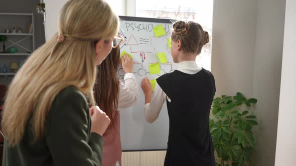 Curios Teenage Girls Sticking Adhesive Notes on Whiteboard Writing Studying Psychology with Teacher