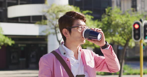 Asian man drinking coffee and using smartphone while crossing the street