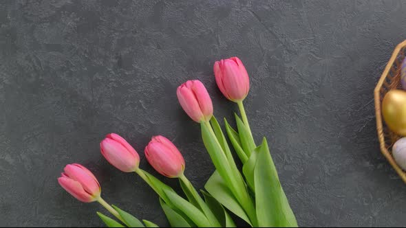 Hands Putting Down Basket with Colorful Easter on a Dark Concrete Table with Tulips