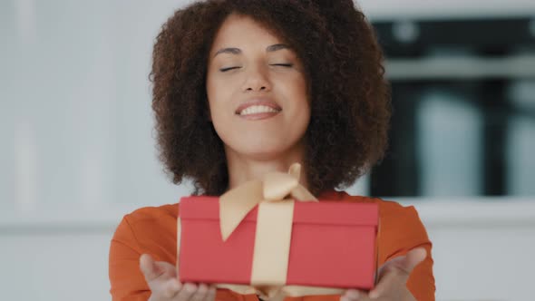 Smiling African American Girl with Curly Hair Holding Giving Present Showing Gift Box Wrapped in Red