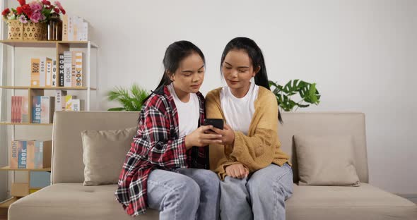Twin girls sitting on couch and shopping online with smartphone at living room