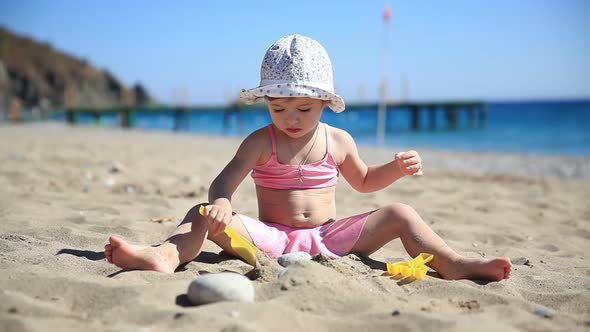 Little Girl in Pink Swimsuit Playing with Sand on the Beach