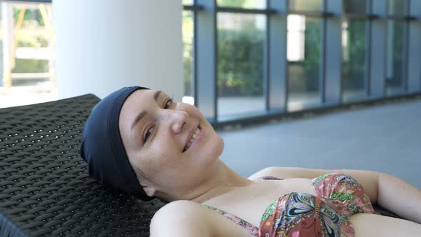 Woman Is Resting Laying on Deckchair in Pool Turning Her Face, Looking at Camera and Smiling.