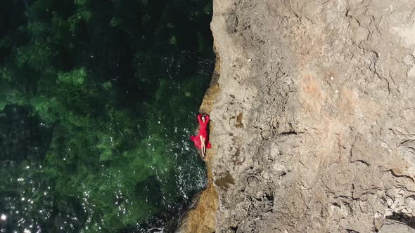 Woman in a Red Long Dress Lies on a Rock