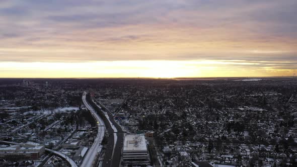 An aerial shot in the suburbs with train tracks and a highway. It was shot at sunrise after a snow s