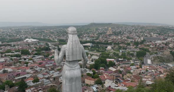 Dolly in aerial shot of the Kartlis Deda monument and Tbilisi cityscape.