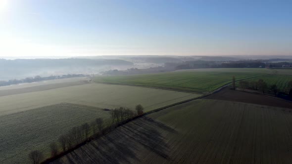 Aerial View of Forest and Farmland During Foggy and Cold Winter Morning with Blue Sky Facing the Sun