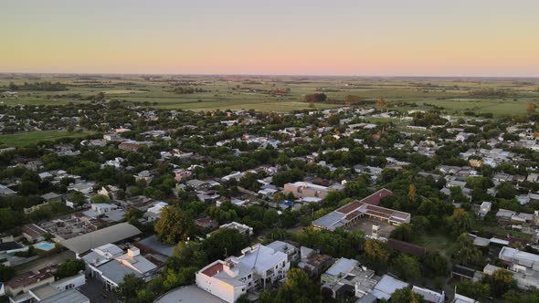 Dolly out flying over Santa Elisa countryside town houses surrounded by trees and farmlands in backg