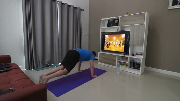 A man in his 30s is doing push ups and oblique exercises in front of a television in his living room