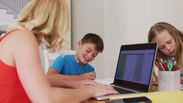 Caucasian mother helping her son with homework while using laptop at home