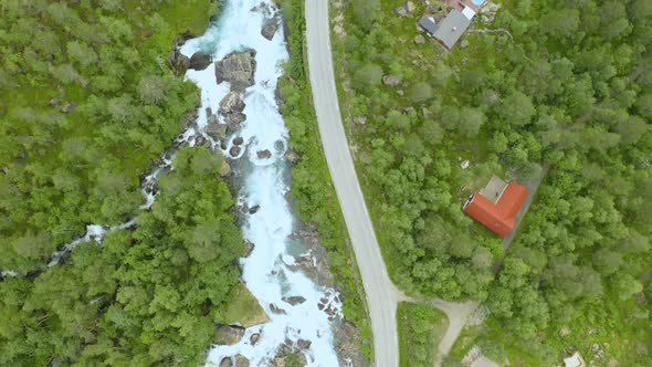 Rocky Stream, Green Forest And Narrow Curved Road In The Countryside In Norway - aerial shot