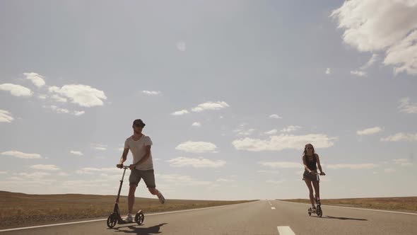 Young People Ride Scooters Around the Empty Field and the Highway