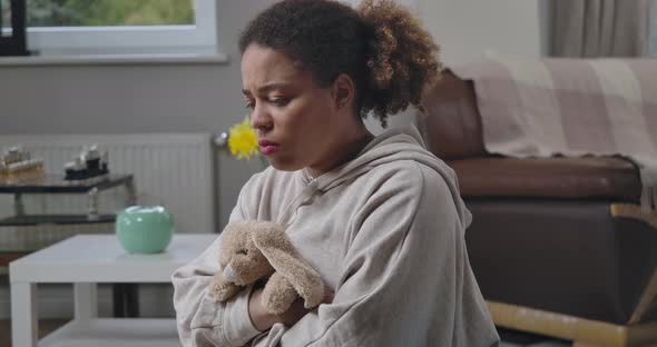 Sad Frustrated African American Woman Sitting at Home Hugging Toy Rabbit