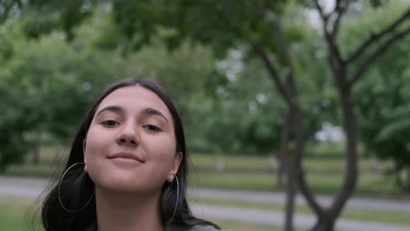 Cheerful Brunette Girl with Long Hair Is Dancing in the Park To the Music While Holding a Portable