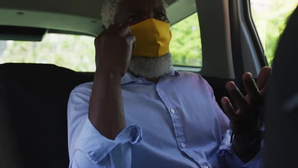 African american senior man wearing face mask talking on smartphone while sitting in the car