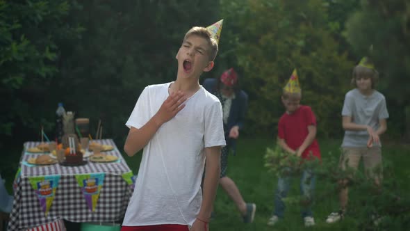 Portrait of Bored Teenage Boy Yawning at Birthday Party with Blurred Group of Friends Dancing at