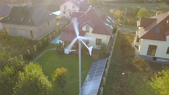 Aerial view of a residential private house with solar panels on roof and wind generator turbine.