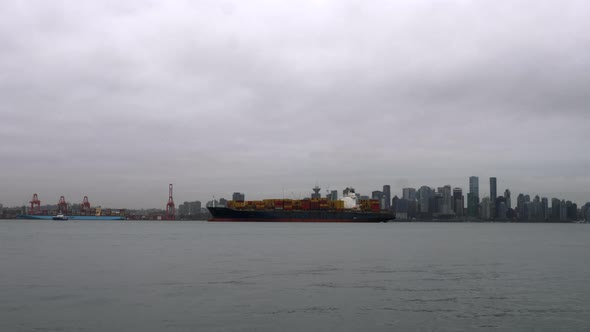 Boats Sailing At Vancouver Harbour Passing By A Container Ship Anchored At The Port On A Cloudy Day