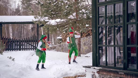 Couple of elves are playing snowballs running aroud a backyard. Holidays. Christmas eve.