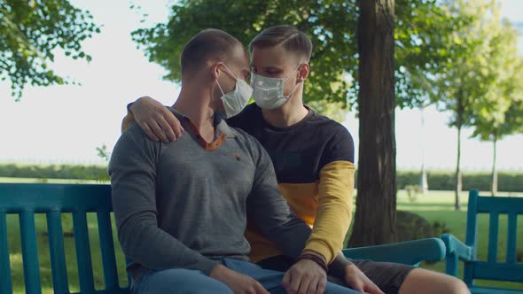 Romantic Gay Couple in Face Masks Sitting on Bench