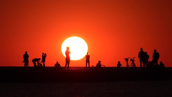 A group of people taking in the sunrise from North Avenue Beach in Chicago with a huge bright sun.