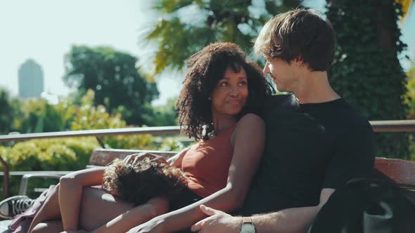 Laughing multiethnic family talking while sitting on the bench in the park