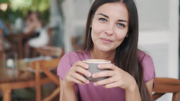 Portrait of Beautiful Woman Drinking Hot Beverage From Cup in Cafe and Smiling