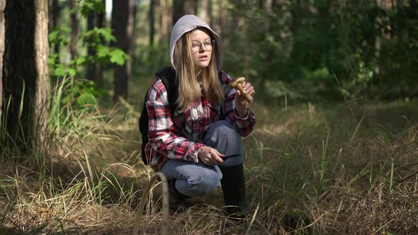 Portrait of Young Confident Woman in Eyeglasses Cutting Mushroom with Knife in Slow Motion Sitting