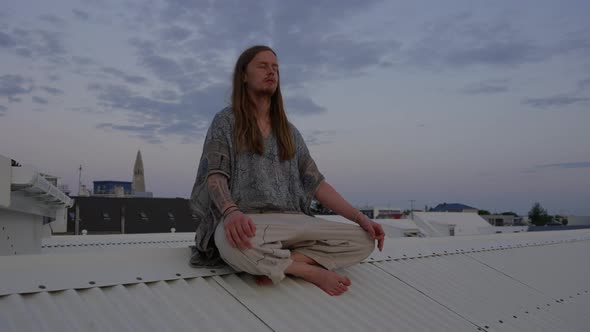 Young Man With Long Hair Meditating On City Roof